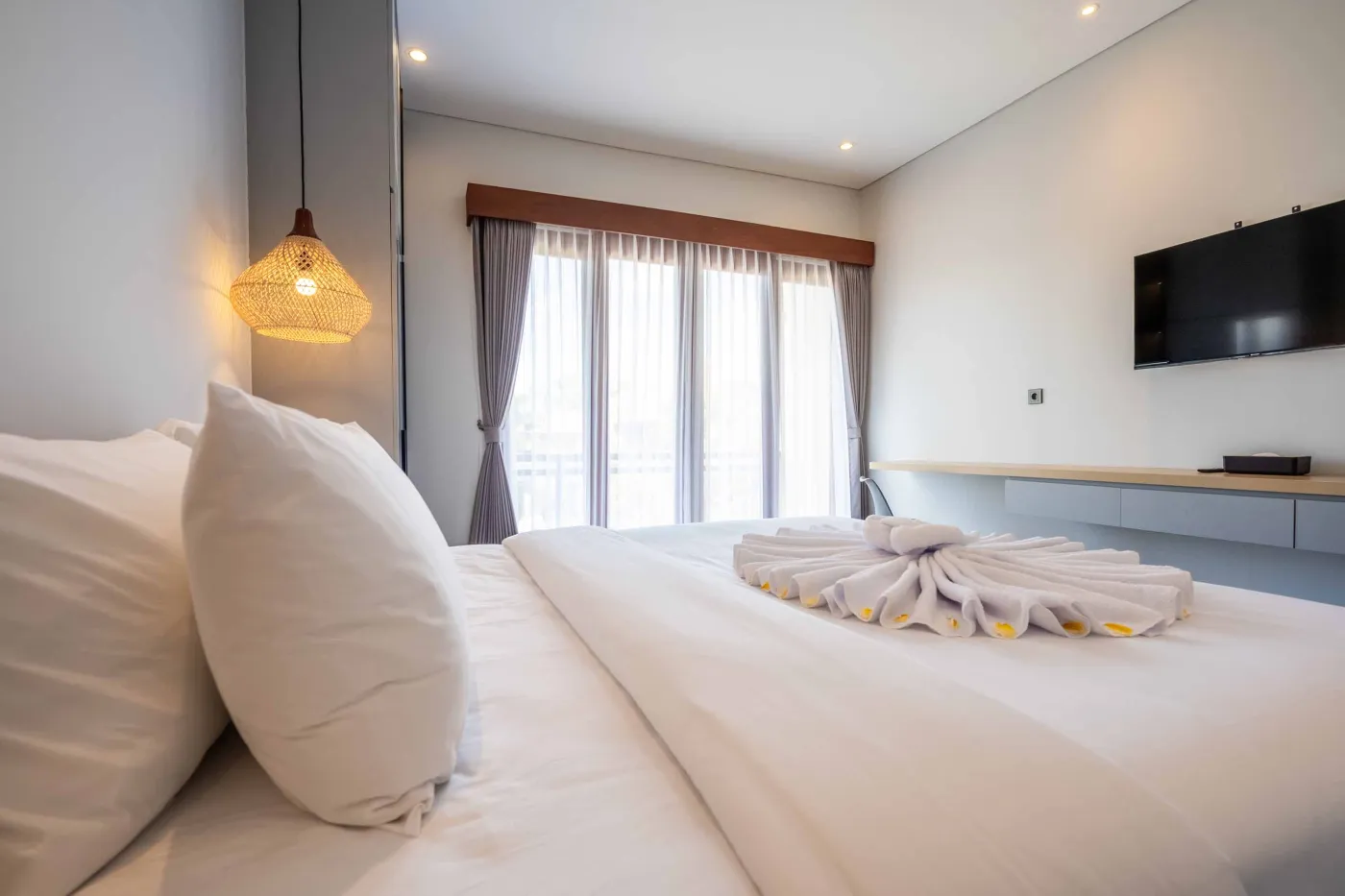 Modern Balinese-style bathroom with glass shower enclosure, round wooden mirror, stone vanity, and stacked towels. - Bali Villas