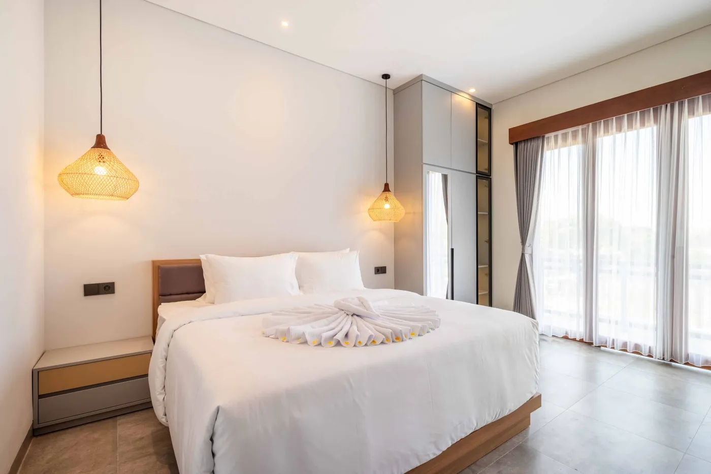 Modern Balinese-style bathroom with glass shower enclosure, round wooden mirror, stone vanity, and stacked towels. - Bali Villas