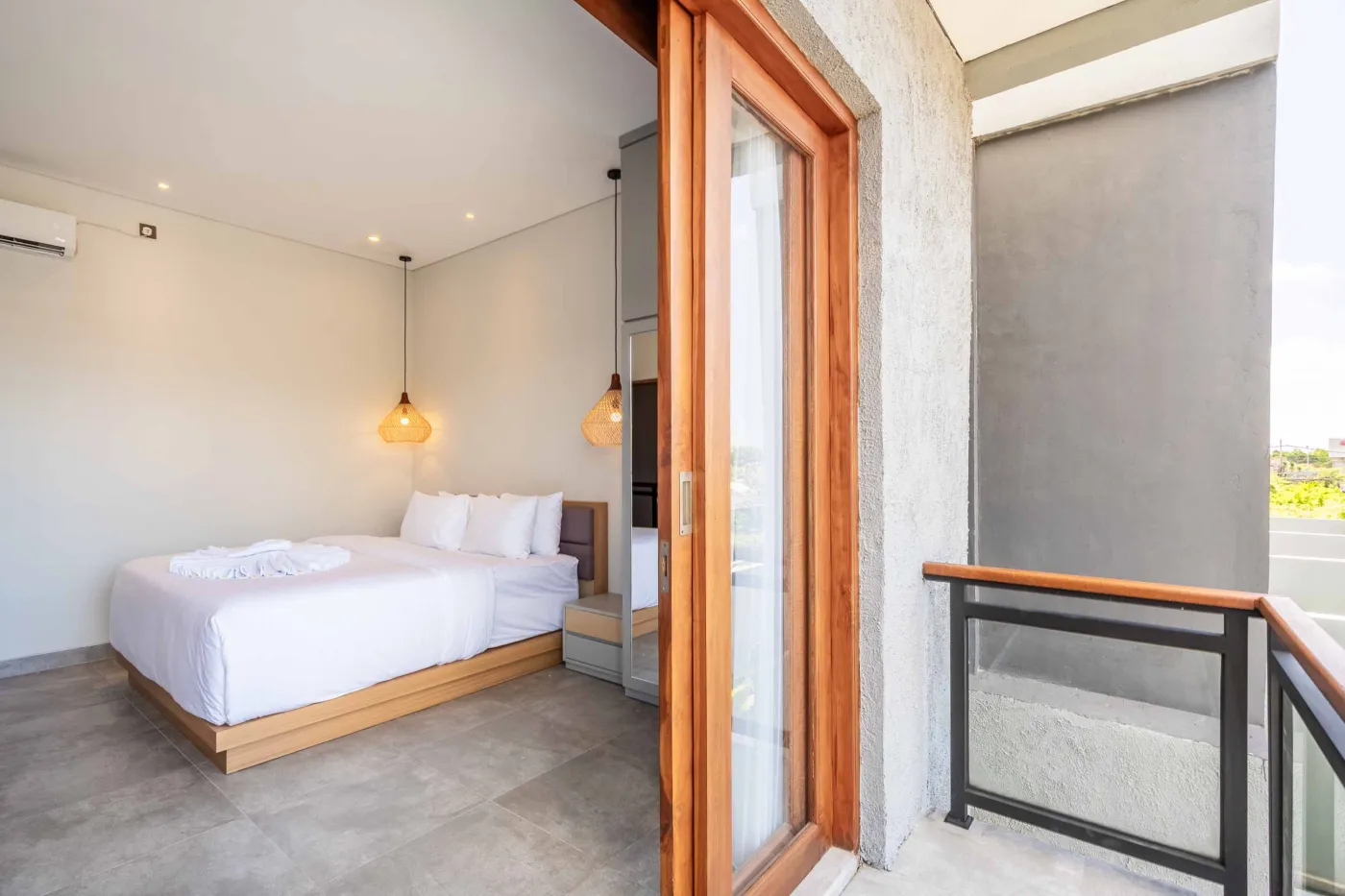 Modern Balinese-style bathroom with glass shower enclosure, round wooden mirror, stone vanity, and stacked towels. - Bali Villas
