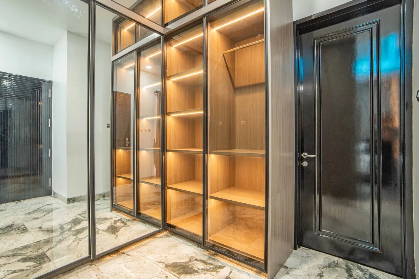 Modern luxury bathroom with LED-lit mirror, wooden vanity sink, white toilet, and beige marble-patterned tiled walls. - Bali Villas