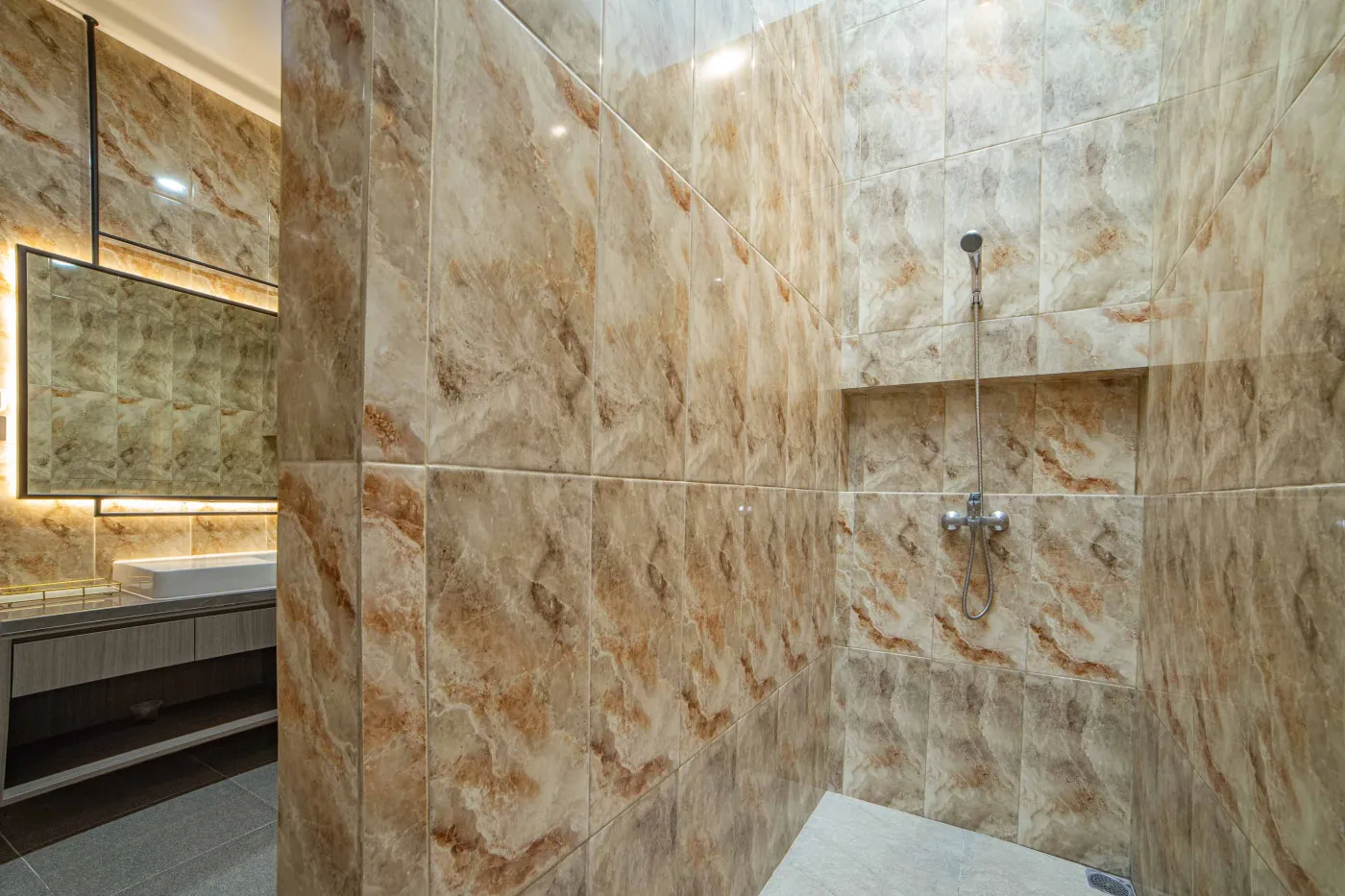 Modern luxury bathroom with LED-lit mirror, wooden vanity sink, white toilet, and beige marble-patterned tiled walls. - Bali Villas