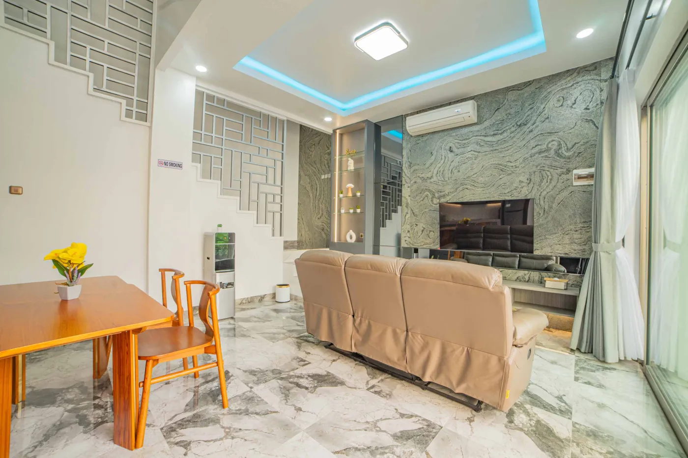 Modern luxury bathroom with LED-lit mirror, wooden vanity sink, white toilet, and beige marble-patterned tiled walls. - Bali Villas