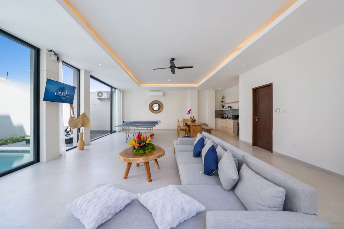 Modern minimalist bathroom interior with light wood vanity, oval mirror, tropical plants, open glass shower enclosure, and neutral tones. - Bali Villas