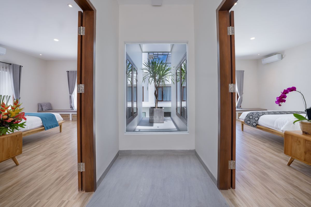 Modern minimalist bathroom interior with light wood vanity, oval mirror, tropical plants, open glass shower enclosure, and neutral tones. - Bali Villas