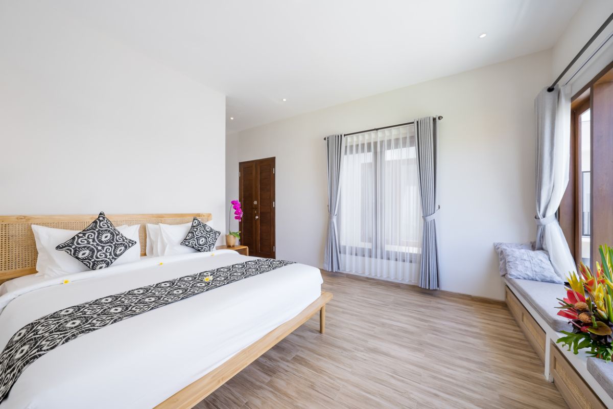 Modern minimalist bathroom interior with light wood vanity, oval mirror, tropical plants, open glass shower enclosure, and neutral tones. - Bali Villas