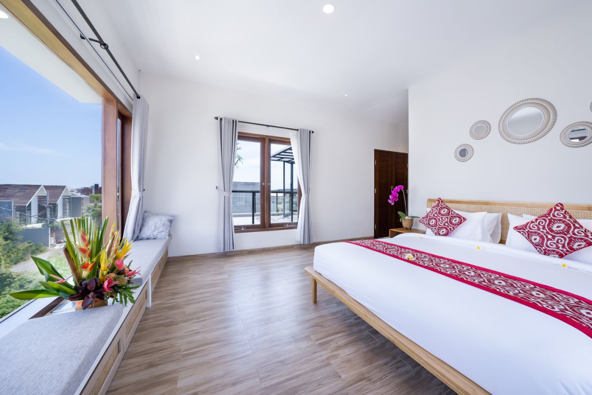 Modern minimalist bathroom interior with light wood vanity, oval mirror, tropical plants, open glass shower enclosure, and neutral tones. - Bali Villas
