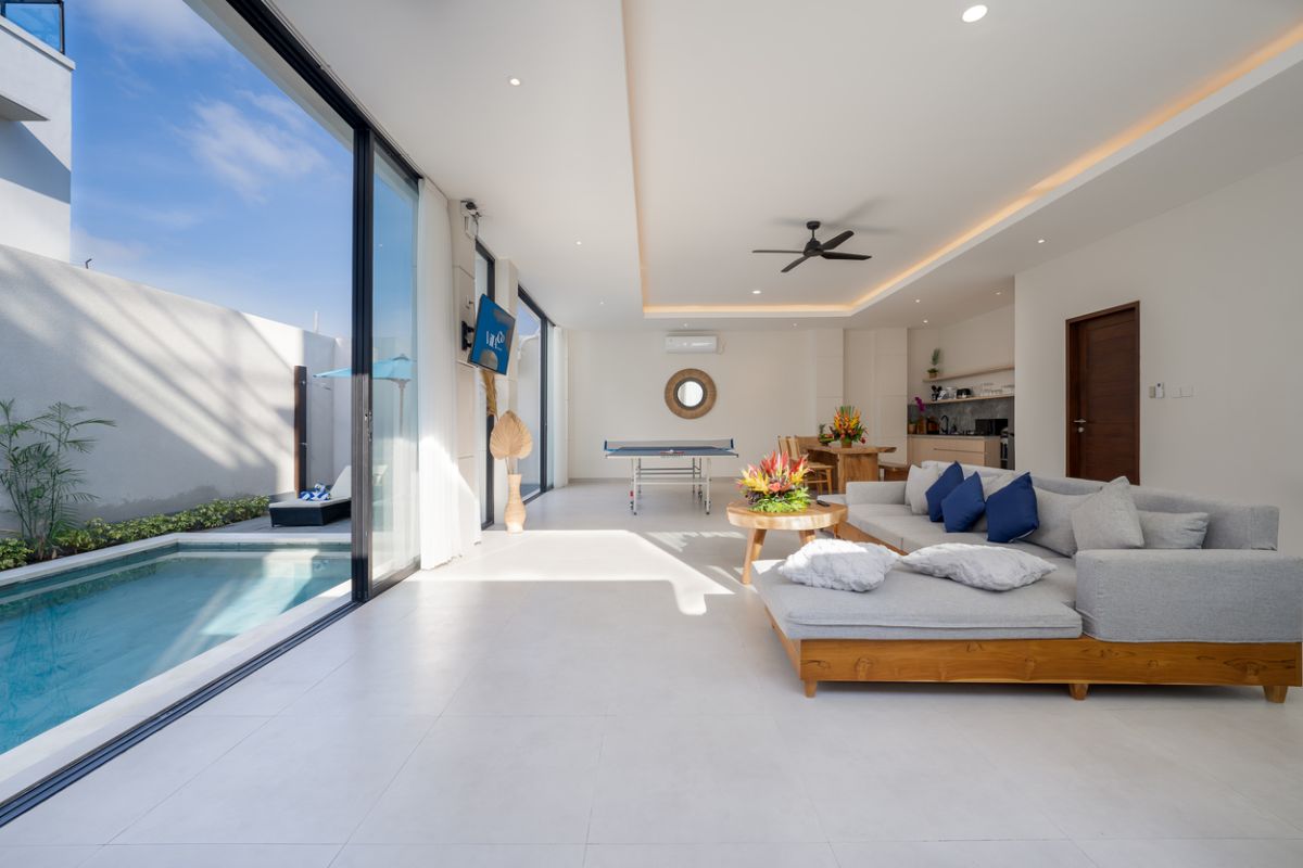Modern minimalist bathroom interior with light wood vanity, oval mirror, tropical plants, open glass shower enclosure, and neutral tones. - Bali Villas