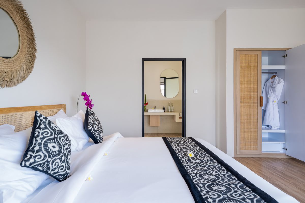 Modern tropical kitchen and dining area with wooden table, rattan chairs, hanging lamps, and infinity pool view through glass doors. - Bali Villas