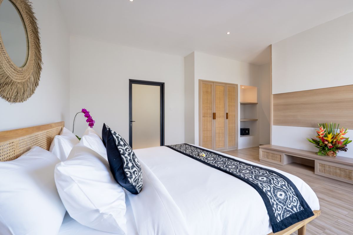 Modern tropical kitchen and dining area with wooden table, rattan chairs, hanging lamps, and infinity pool view through glass doors. - Bali Villas