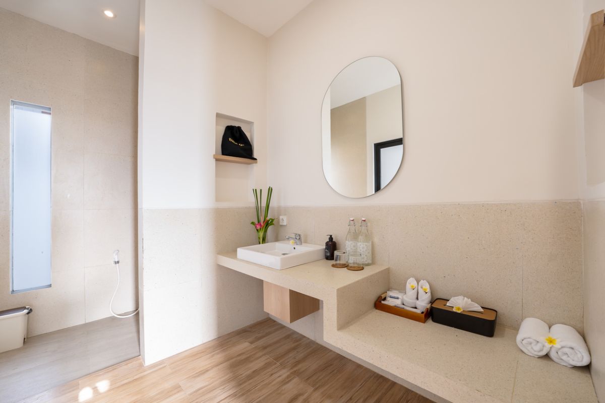 Modern tropical kitchen and dining area with wooden table, rattan chairs, hanging lamps, and infinity pool view through glass doors. - Bali Villas