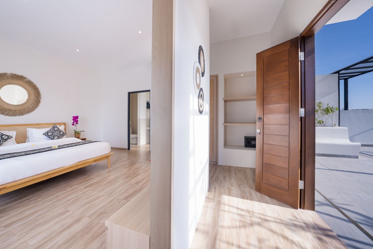 Modern tropical kitchen and dining area with wooden table, rattan chairs, hanging lamps, and infinity pool view through glass doors. - Bali Villas
