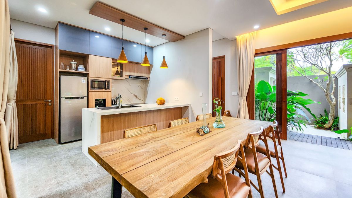 Tropical Balinese outdoor lounge with blue cushions on wooden deck, bamboo pergola, ceiling fan, lush greenery, and turquoise plunge pool. - Bali Villas
