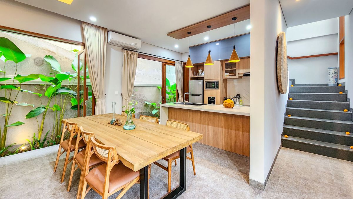 Tropical Balinese outdoor lounge with blue cushions on wooden deck, bamboo pergola, ceiling fan, lush greenery, and turquoise plunge pool. - Bali Villas