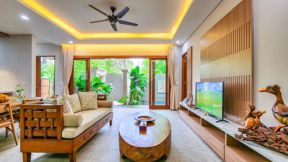 Tropical Balinese outdoor lounge with blue cushions on wooden deck, bamboo pergola, ceiling fan, lush greenery, and turquoise plunge pool. - Bali Villas