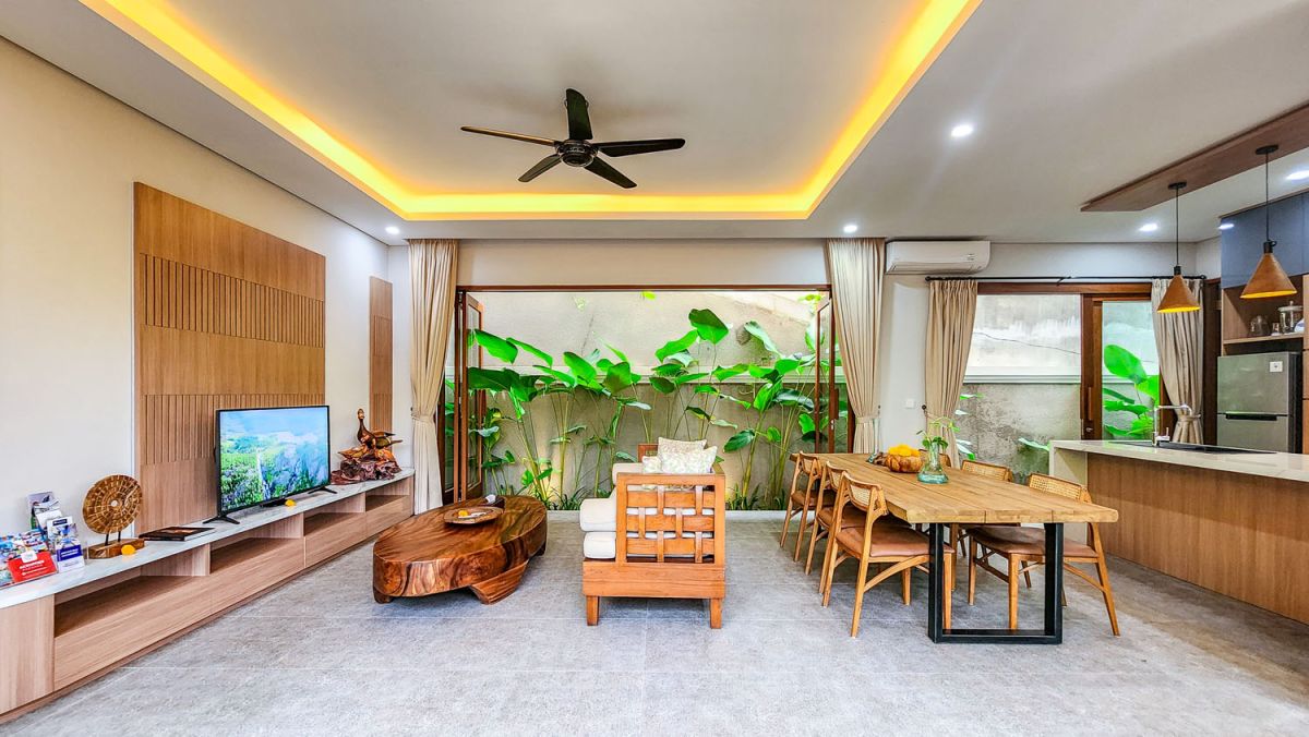 Tropical Balinese outdoor lounge with blue cushions on wooden deck, bamboo pergola, ceiling fan, lush greenery, and turquoise plunge pool. - Bali Villas