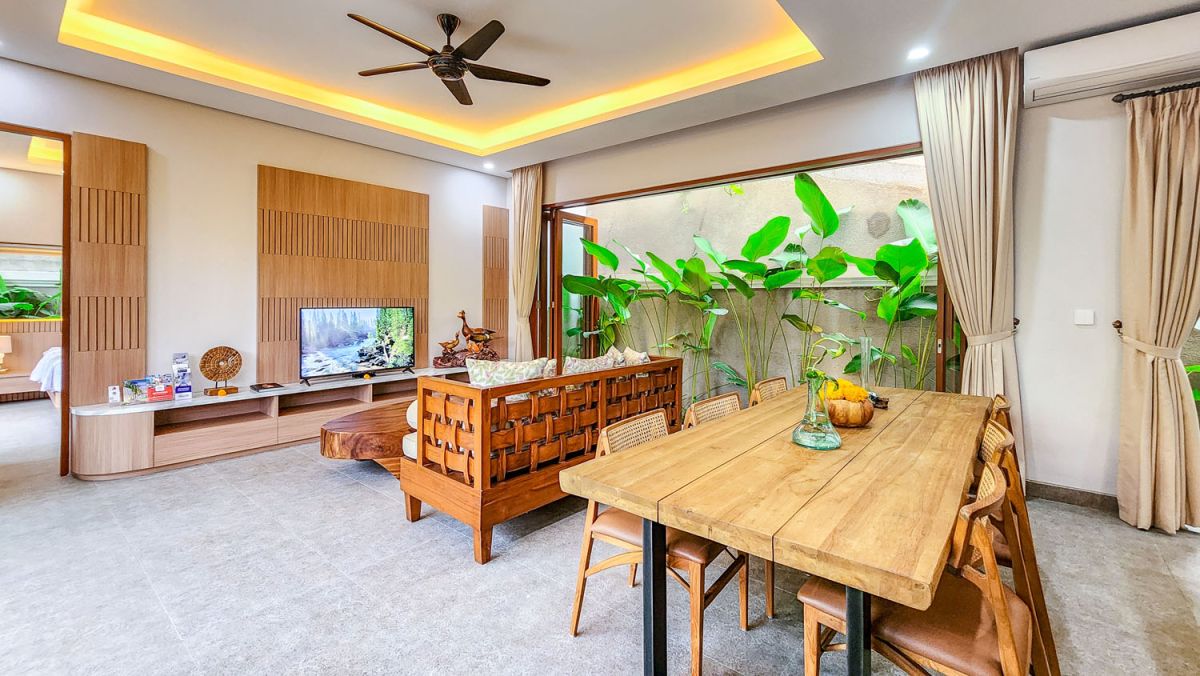 Tropical Balinese outdoor lounge with blue cushions on wooden deck, bamboo pergola, ceiling fan, lush greenery, and turquoise plunge pool. - Bali Villas
