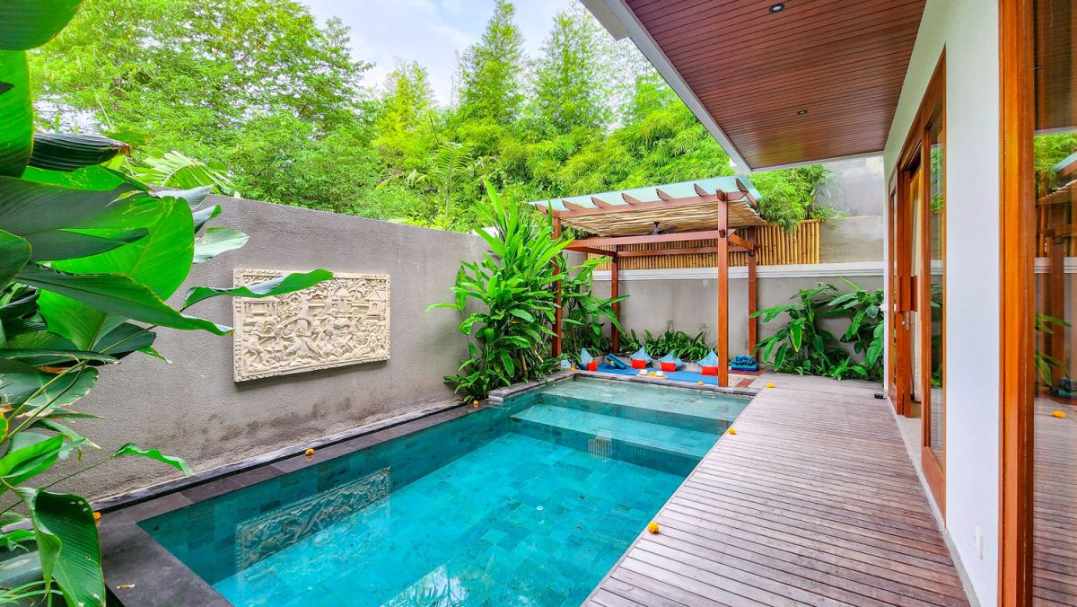 Tropical Balinese outdoor lounge with blue cushions on wooden deck, bamboo pergola, ceiling fan, lush greenery, and turquoise plunge pool. - Bali Villas
