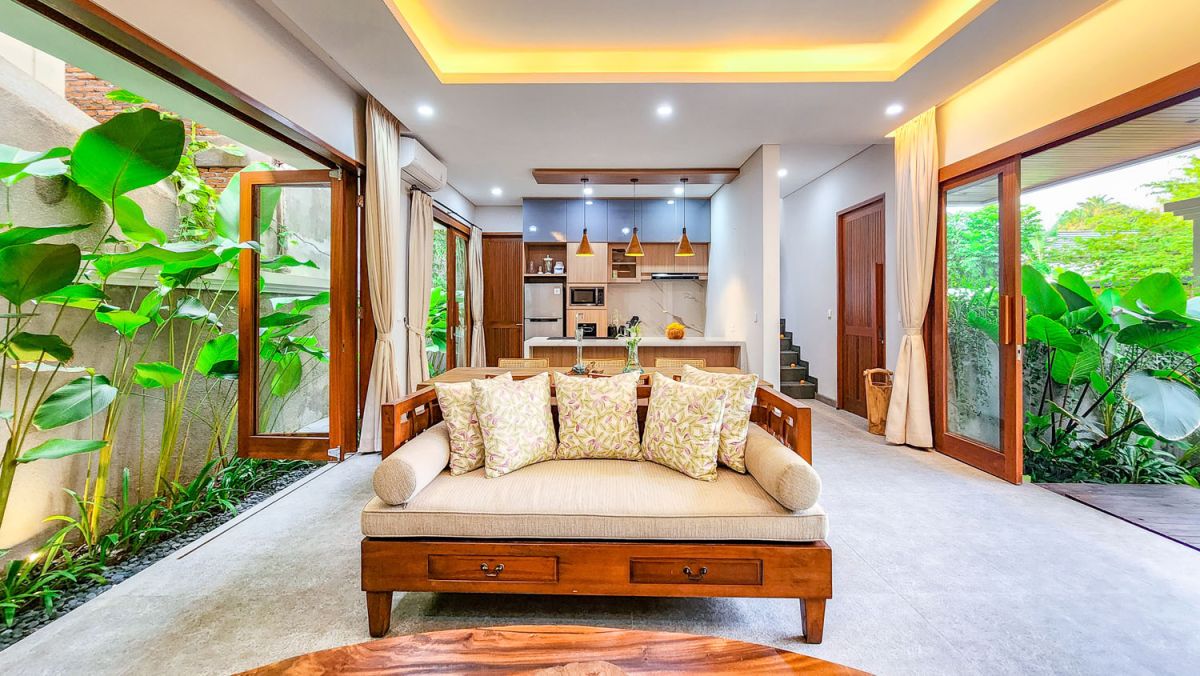 Tropical Balinese outdoor lounge with blue cushions on wooden deck, bamboo pergola, ceiling fan, lush greenery, and turquoise plunge pool. - Bali Villas