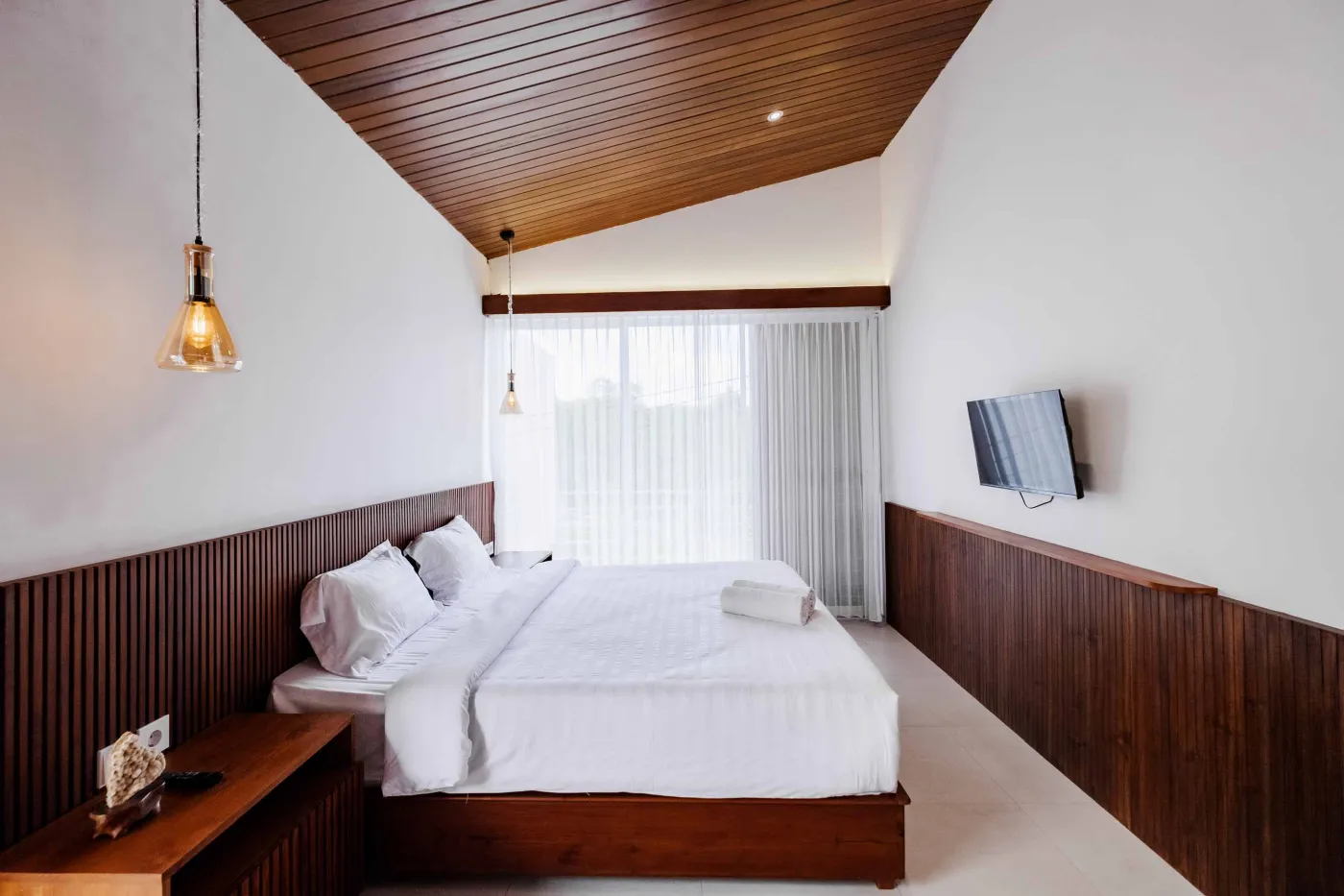 Modern bathroom with white freestanding tub, glass-enclosed teal-tiled shower, white toilet, and wooden shutters overlooking greenery. - Bali Villas