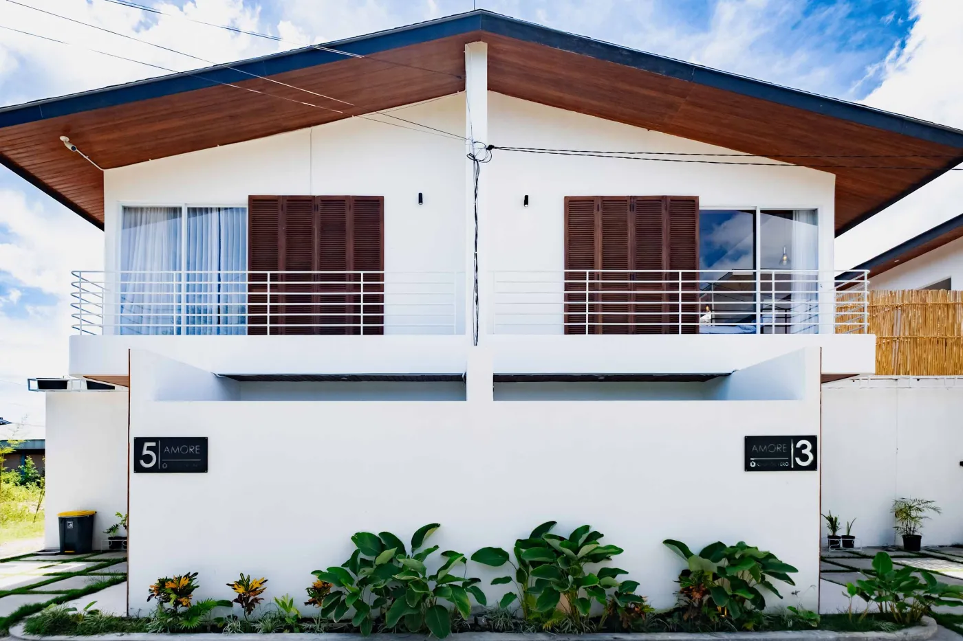 Modern bathroom with white freestanding tub, glass-enclosed teal-tiled shower, white toilet, and wooden shutters overlooking greenery. - Bali Villas