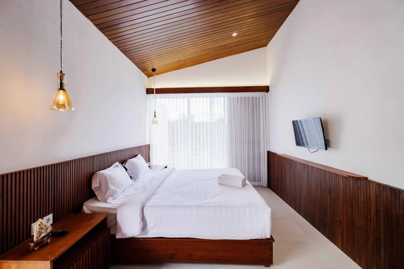 Modern bathroom with white freestanding tub, glass-enclosed teal-tiled shower, white toilet, and wooden shutters overlooking greenery. - Bali Villas