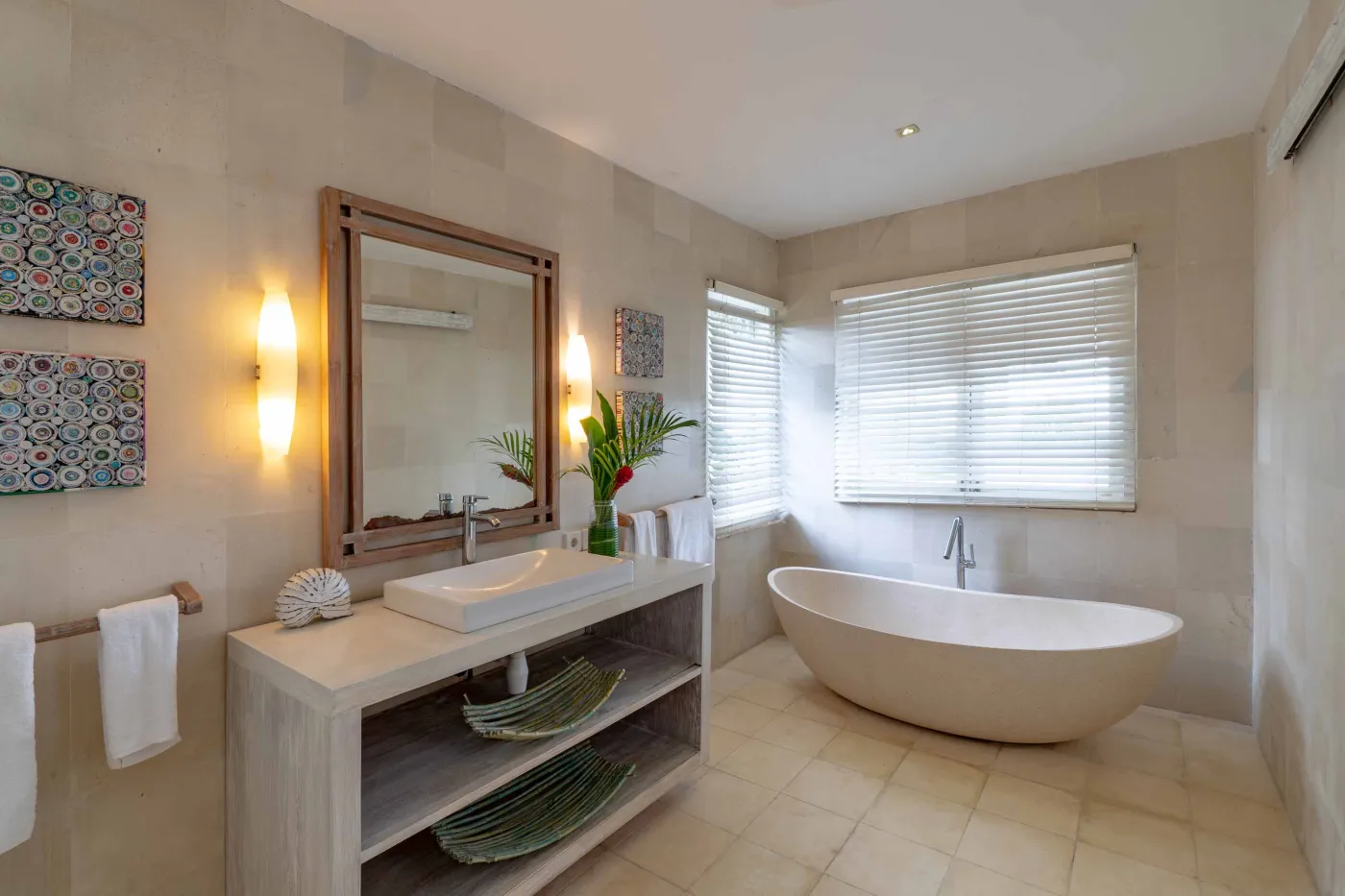 Spacious modern Balinese-style kitchen with high wooden ceiling, rattan pendant lights, white island bar, fresh fruits, and tropical garden views through large windows. - Bali Villas