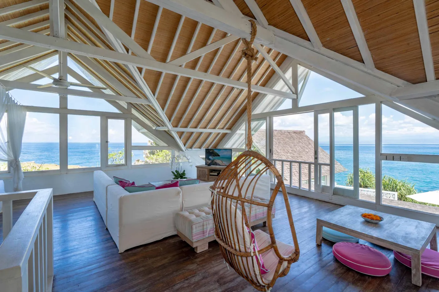 Spacious modern Balinese-style kitchen with high wooden ceiling, rattan pendant lights, white island bar, fresh fruits, and tropical garden views through large windows. - Bali Villas