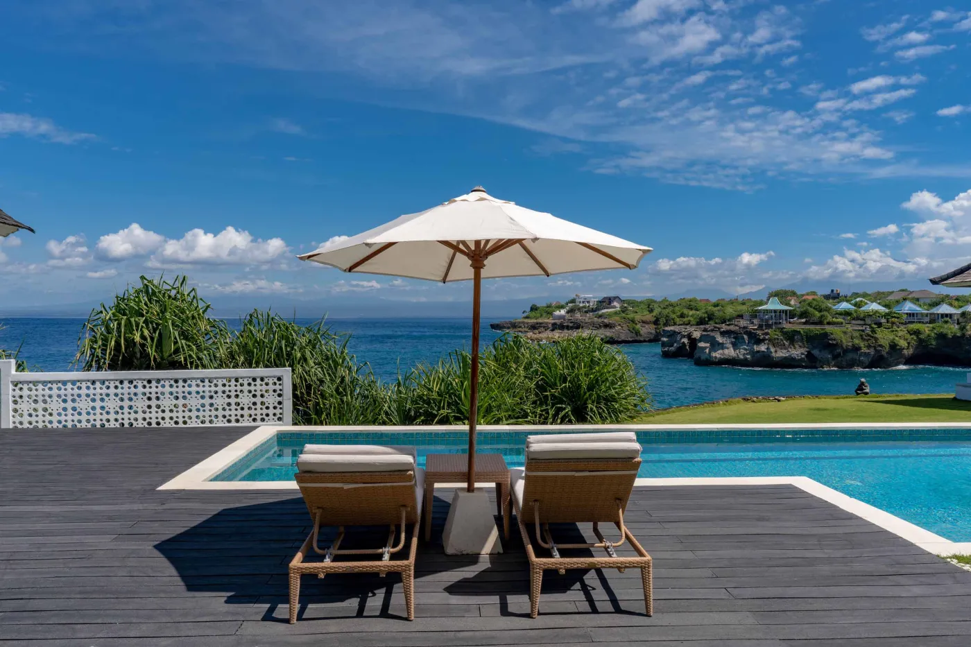 Spacious modern Balinese-style kitchen with high wooden ceiling, rattan pendant lights, white island bar, fresh fruits, and tropical garden views through large windows. - Bali Villas