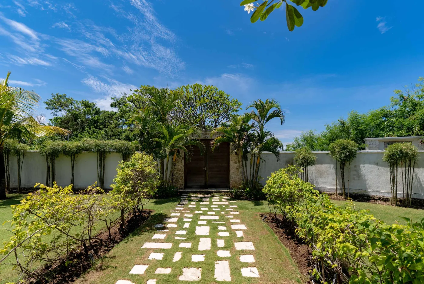 Spacious modern Balinese-style kitchen with high wooden ceiling, rattan pendant lights, white island bar, fresh fruits, and tropical garden views through large windows. - Bali Villas