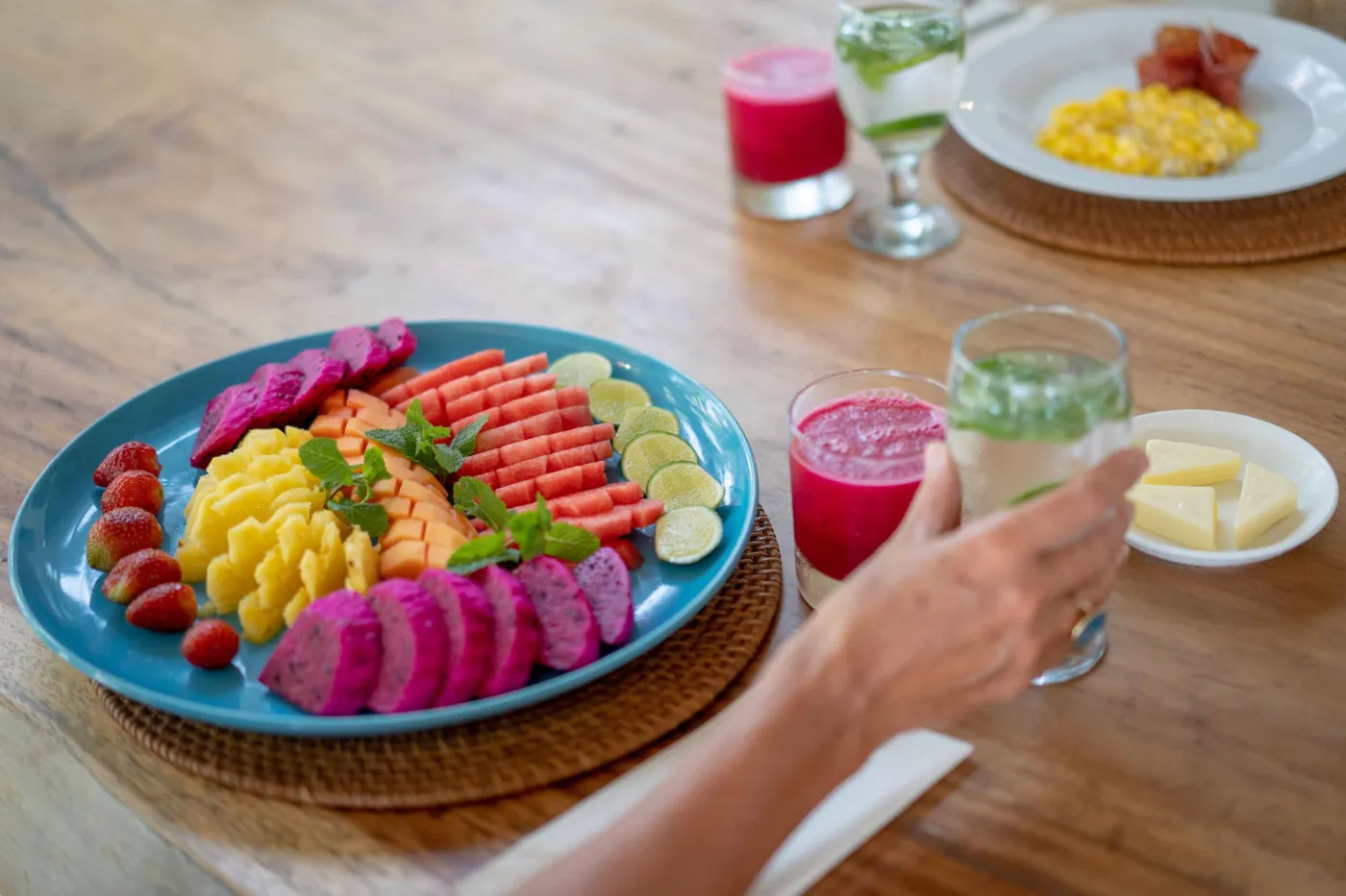 Spacious modern Balinese-style kitchen with high wooden ceiling, rattan pendant lights, white island bar, fresh fruits, and tropical garden views through large windows. - Bali Villas