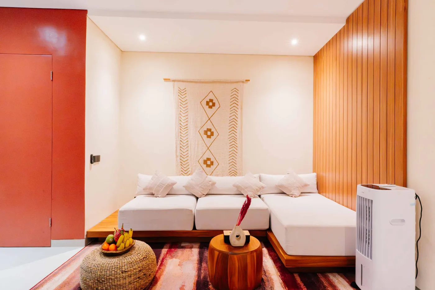 Compact white-tiled bathroom with round black mirror, woven pendant light, frangipani flowers on shelf, white sink, toilet, and folded towels. - Bali Villas