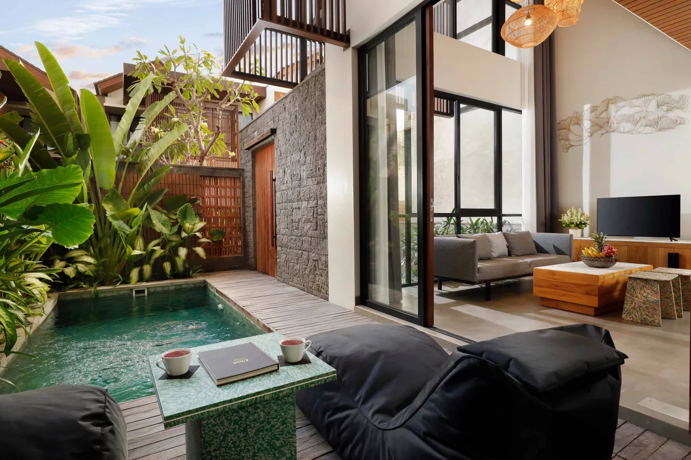 Serene tropical villa patio with private plunge pool, plush lounge seating, coffee table, and sliding doors to modern indoor living area amid lush greenery. - Bali Villas