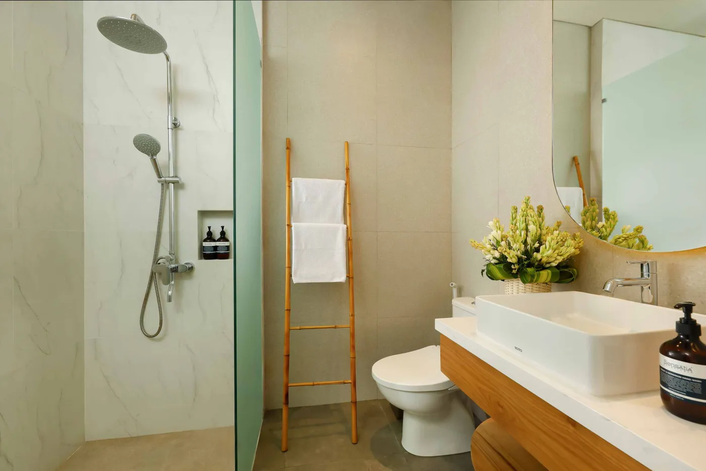 Modern spa bathroom featuring wooden vanity with round sink, oval mirror, white toilet, and petal-filled freestanding tub. - Bali Villas