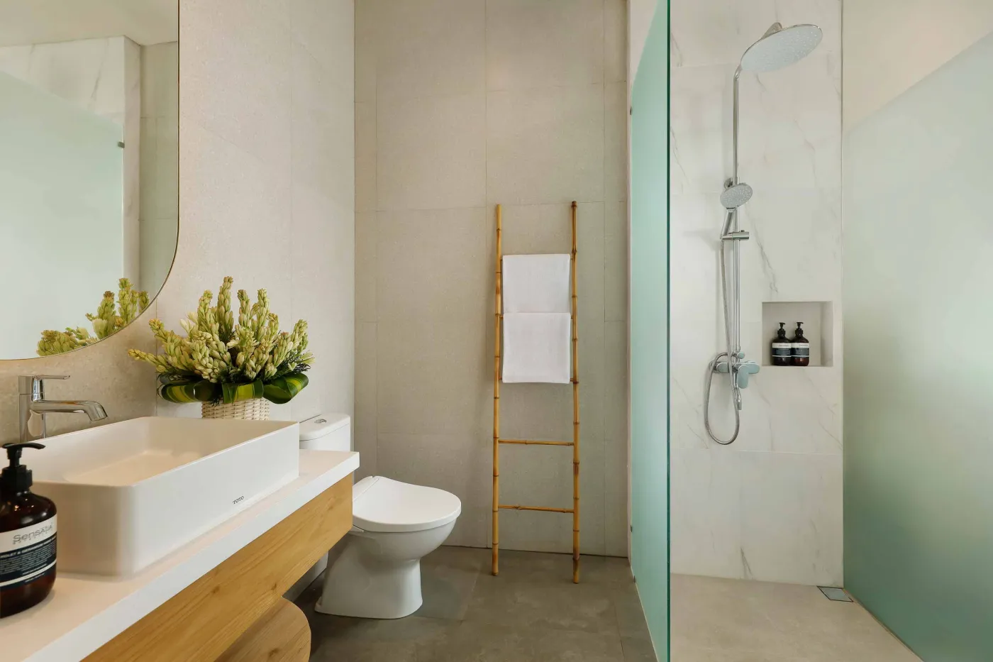 Modern spa bathroom featuring wooden vanity with round sink, oval mirror, white toilet, and petal-filled freestanding tub. - Bali Villas