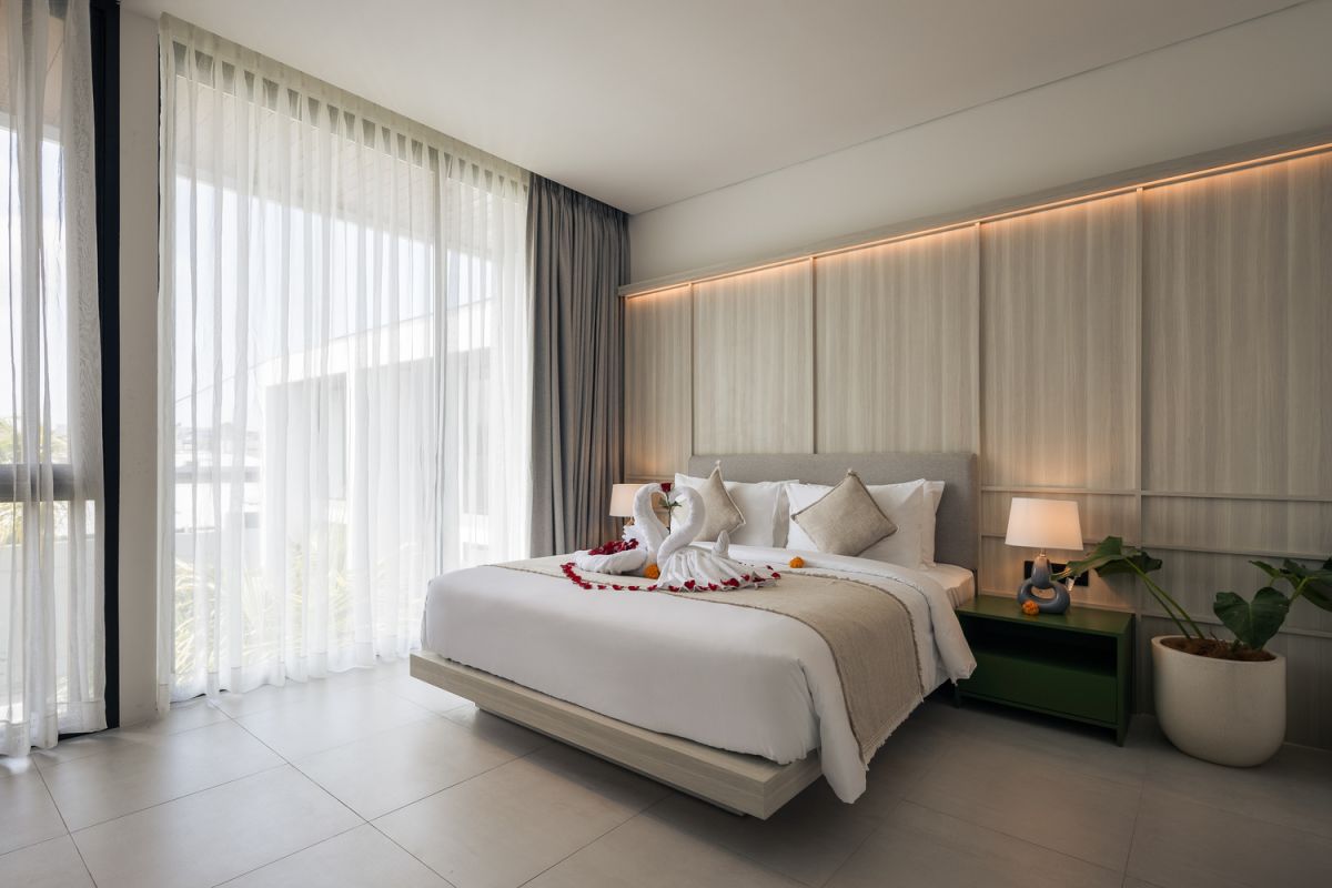 Modern open-plan kitchen and living room interior with vertical green wall, wooden staircase, bar stools, and plush green sofa against white marble flooring. - Bali Villas