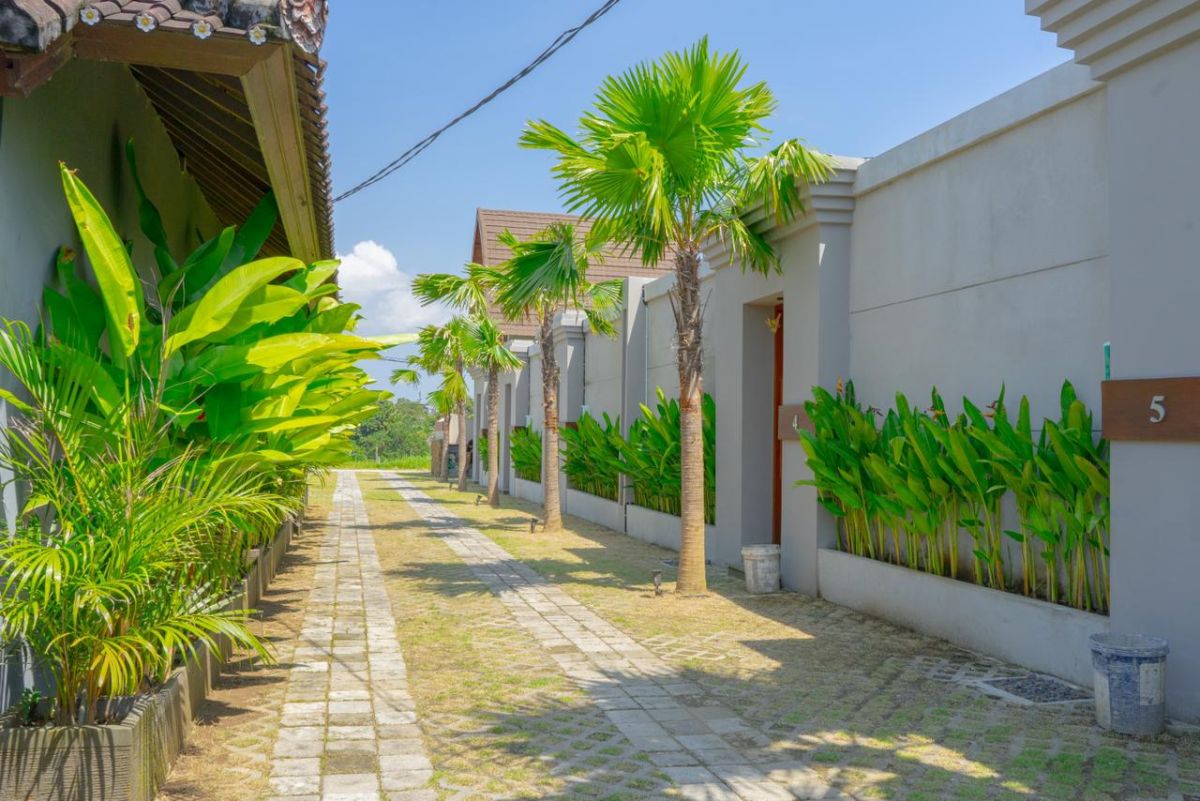 Modern interior with white bathtub and open archway leading to a private blue infinity pool, wooden lounge chairs, hanging lantern, and lush green vines in a serene courtyard. - Bali Villas