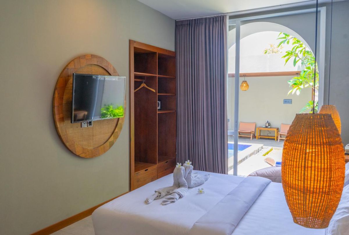 Modern interior with white bathtub and open archway leading to a private blue infinity pool, wooden lounge chairs, hanging lantern, and lush green vines in a serene courtyard. - Bali Villas