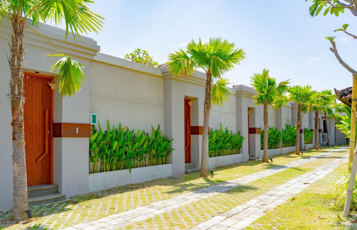 Modern interior with white bathtub and open archway leading to a private blue infinity pool, wooden lounge chairs, hanging lantern, and lush green vines in a serene courtyard. - Bali Villas
