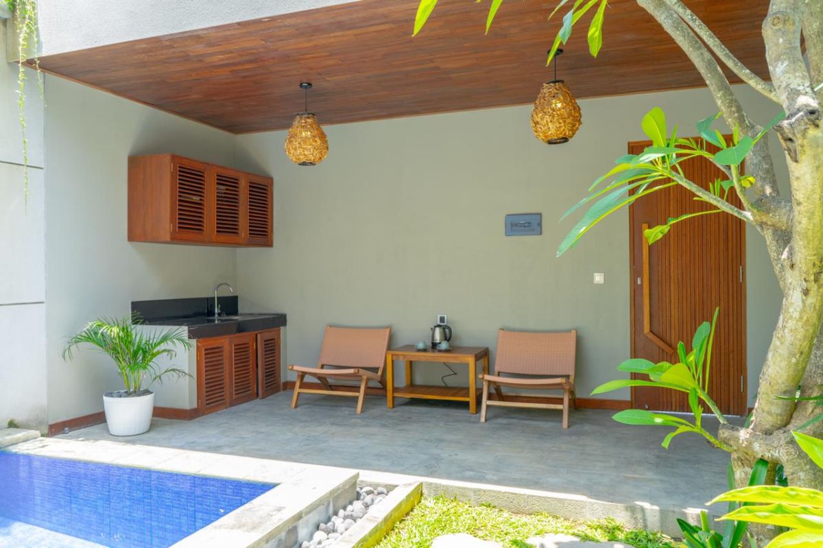 Modern interior with white bathtub and open archway leading to a private blue infinity pool, wooden lounge chairs, hanging lantern, and lush green vines in a serene courtyard. - Bali Villas