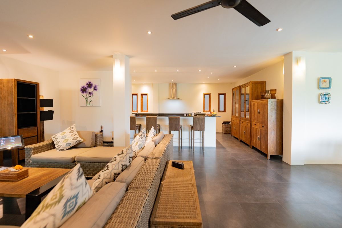 Modern open-plan kitchen with white cabinets, black granite island, stainless steel appliances, and tropical wood accents. - Bali Villas