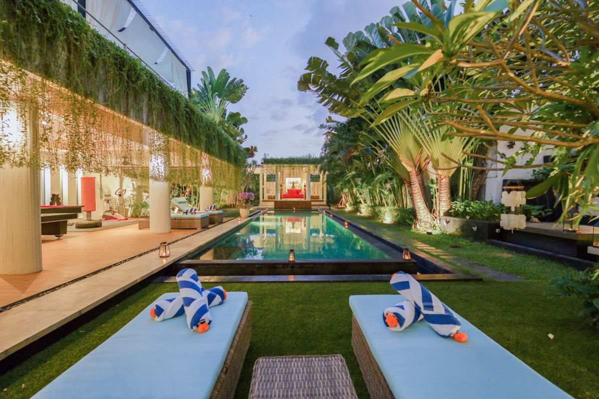 Modern open-plan kitchen with white cabinets, black granite island, stainless steel appliances, and tropical wood accents. - Bali Villas
