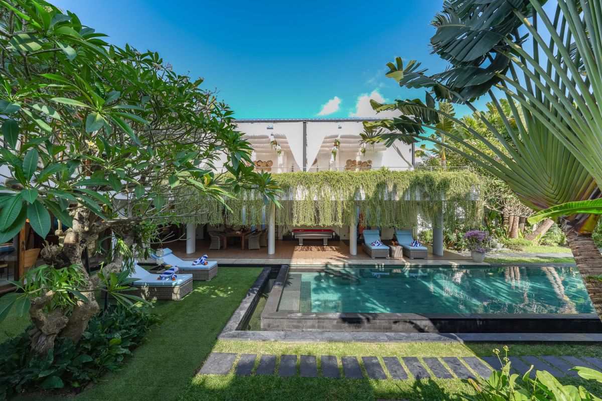 Modern open-plan kitchen with white cabinets, black granite island, stainless steel appliances, and tropical wood accents. - Bali Villas