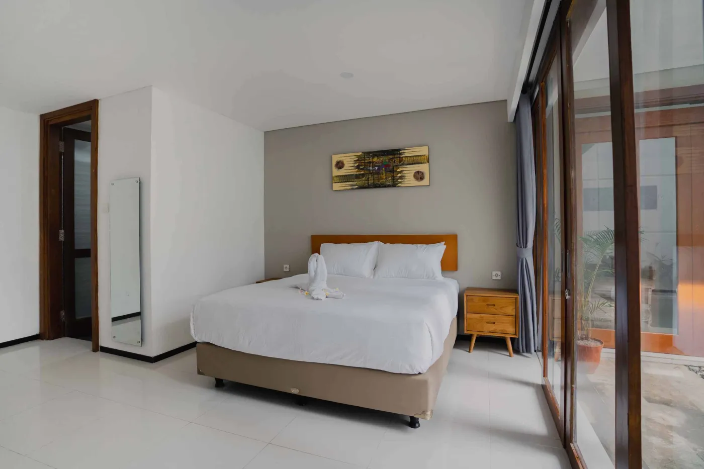 Modern bathroom with white toilet, sink vanity, wooden wardrobe, and round mirror on white brick walls. - Bali Villas