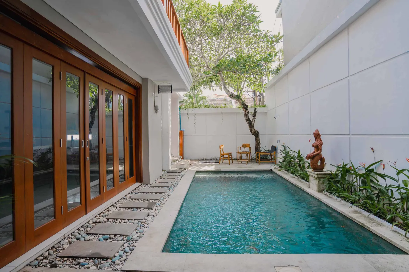 Modern bathroom with white toilet, sink vanity, wooden wardrobe, and round mirror on white brick walls. - Bali Villas