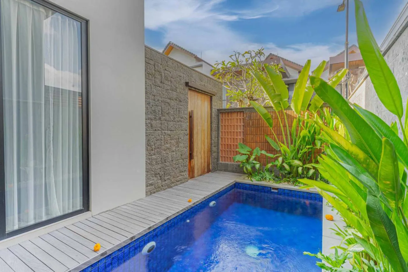 Woven bamboo pendant lights hanging in a modern tropical room with gray curtains, wooden shelves, and infinity pool view. - Bali Villas