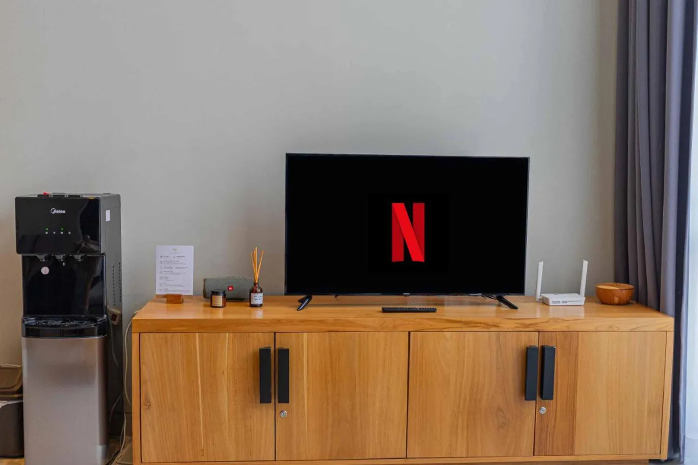 Woven bamboo pendant lights hanging in a modern tropical room with gray curtains, wooden shelves, and infinity pool view. - Bali Villas