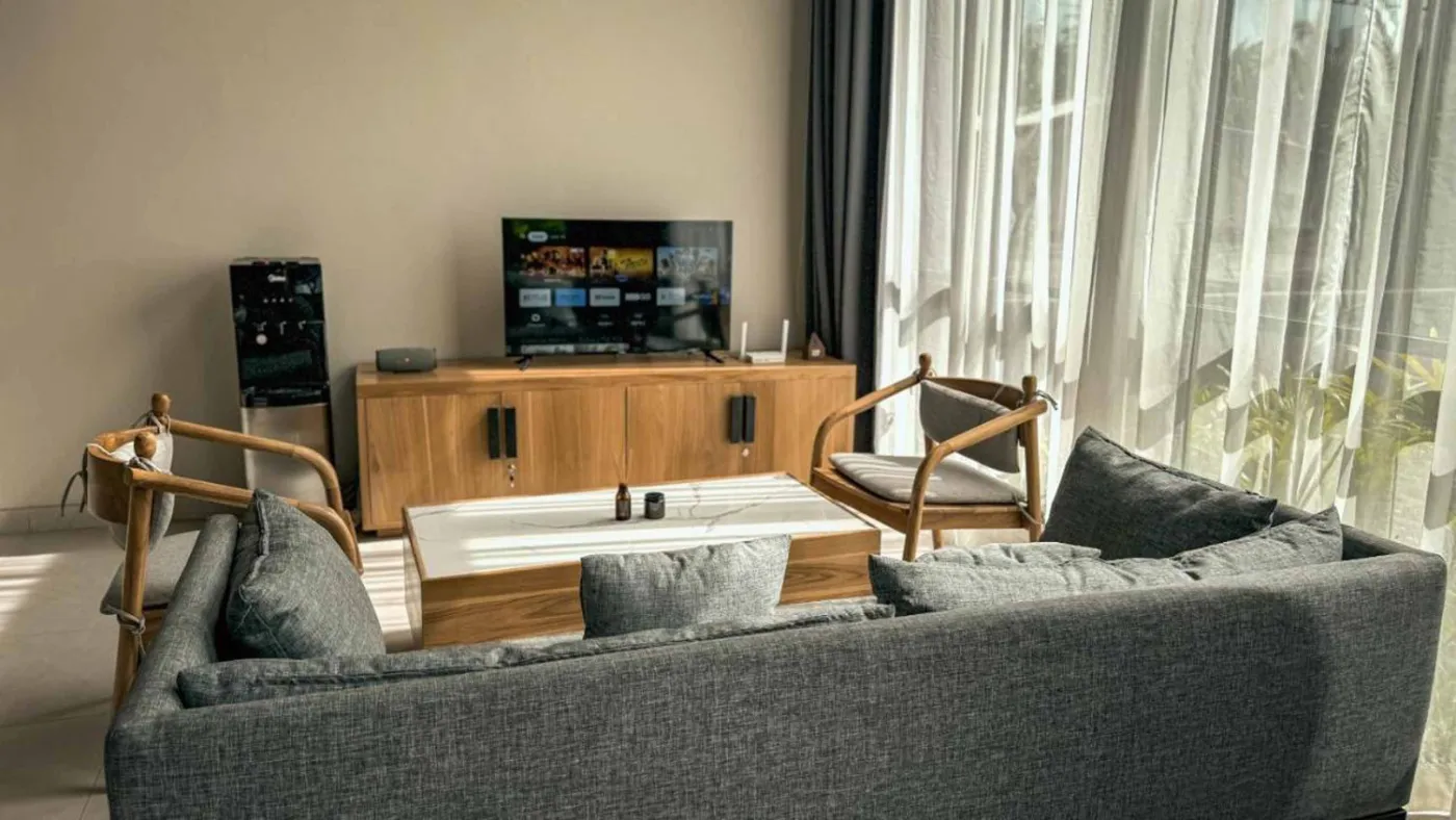Woven bamboo pendant lights hanging in a modern tropical room with gray curtains, wooden shelves, and infinity pool view. - Bali Villas