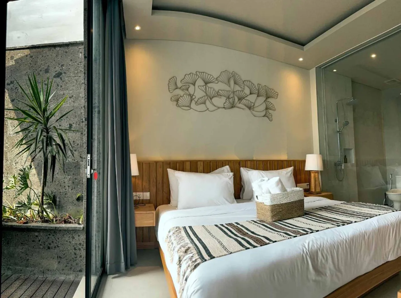 Woven bamboo pendant lights hanging in a modern tropical room with gray curtains, wooden shelves, and infinity pool view. - Bali Villas