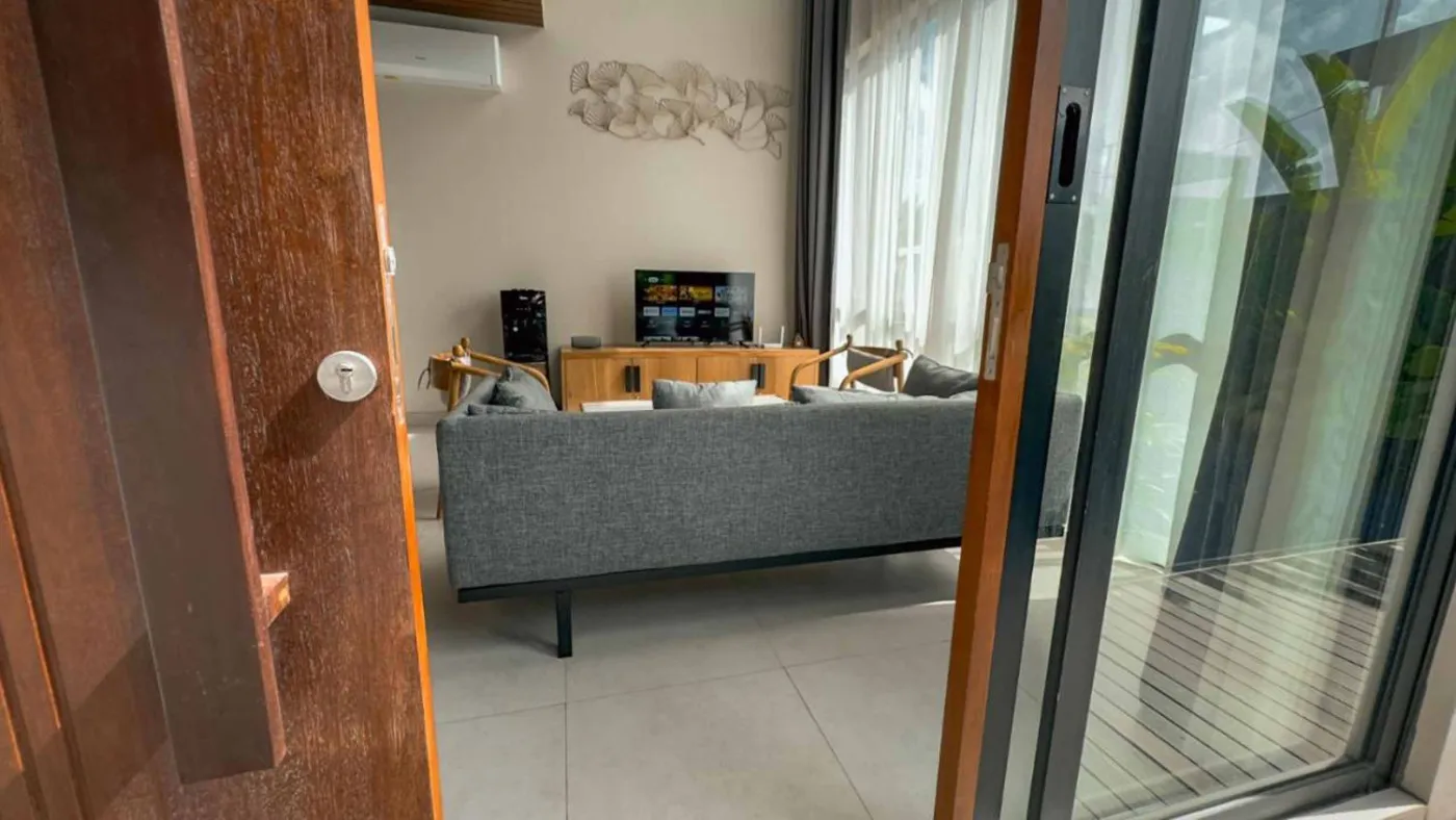 Woven bamboo pendant lights hanging in a modern tropical room with gray curtains, wooden shelves, and infinity pool view. - Bali Villas