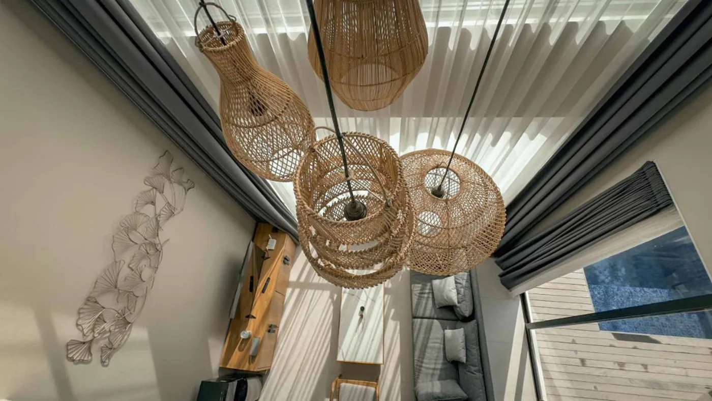 Woven bamboo pendant lights hanging in a modern tropical room with gray curtains, wooden shelves, and infinity pool view. - Bali Villas